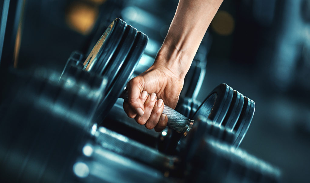 Closeup side view of unrecognizable woman grabbing a dumbbell from a dumbbell rack. Shallow focus, toned image.