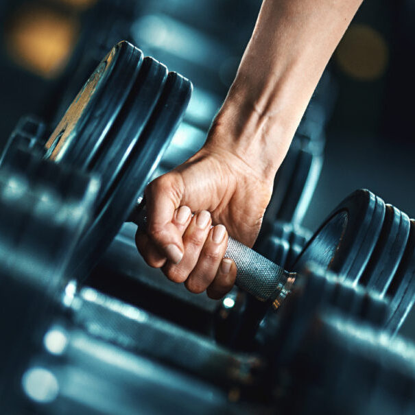 Closeup side view of unrecognizable woman grabbing a dumbbell from a dumbbell rack. Shallow focus, toned image.